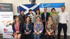 A group of diverse individuals poses in front of an "International Students" banner, with a Scottish flag in the background.