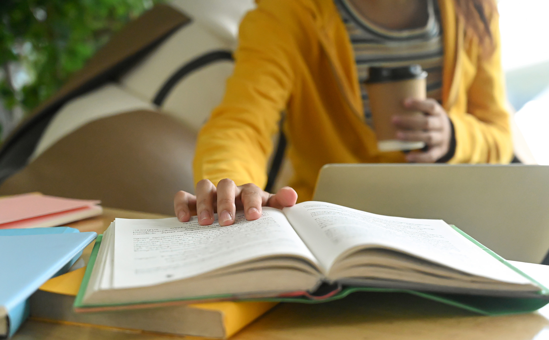 Person holding a coffee cup is holding open a page on a book. 