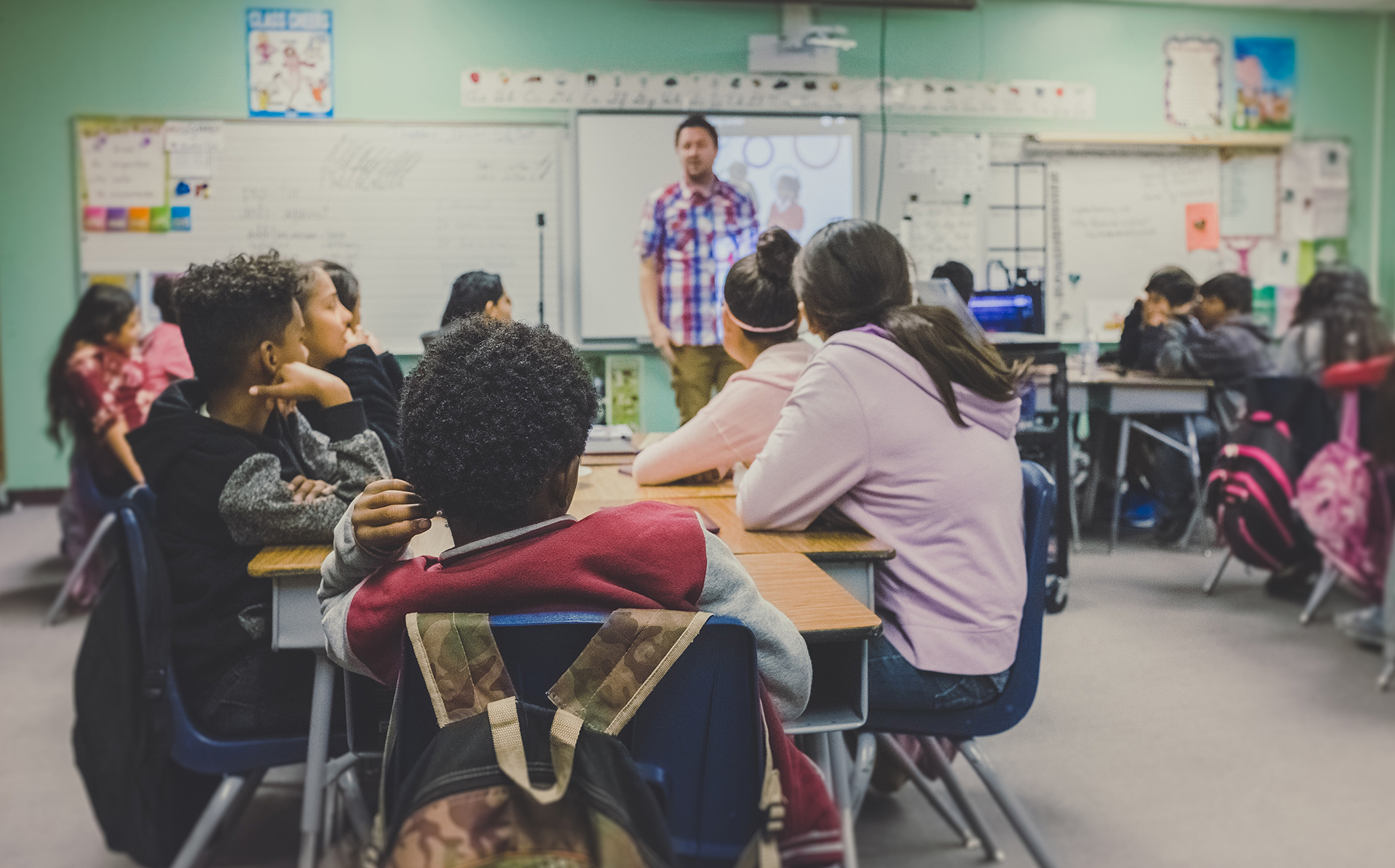 Classroom of young students looking towards their teacher. Several white boards are in the background.