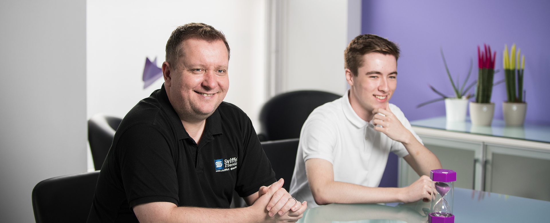 Young student working at a desk in an open plan office during a work placement next to their mentor.