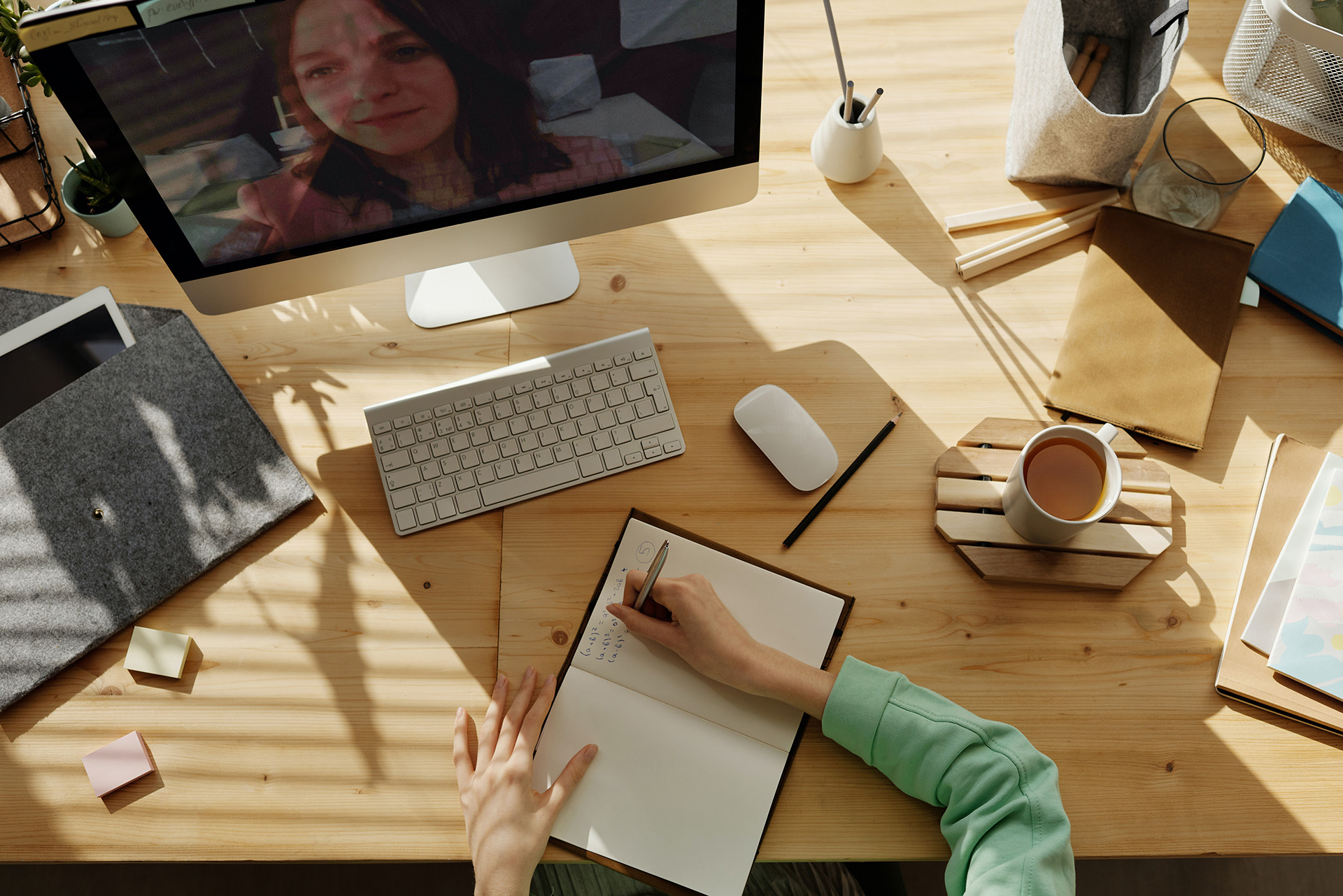 Person writing notes at their desk with their computer on and a cup of coffee next to them.