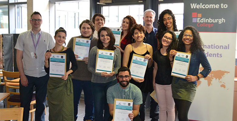 A diverse group of students proudly holds certificates, celebrating their achievements in an indoor setting.