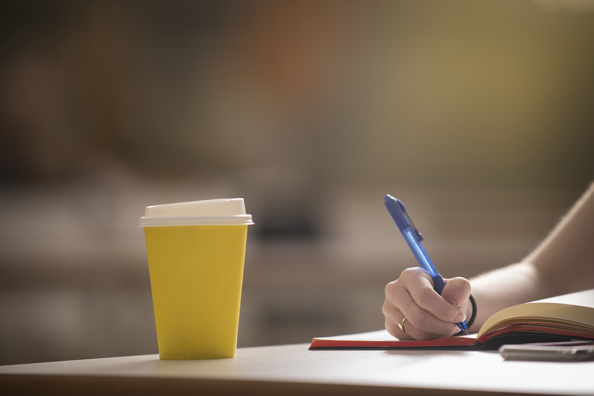 Disposable yellow coffee cup on a desk while a student is taking notes in a notebook.