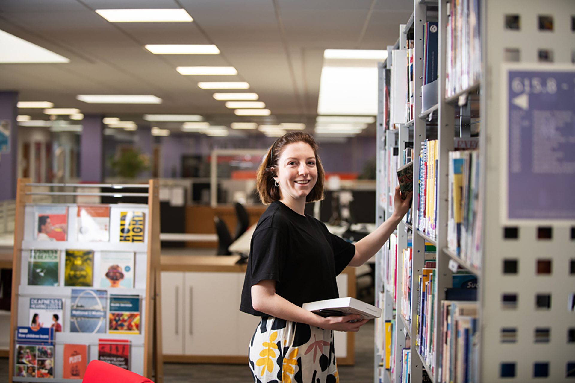 Student picking out a book from a library shelf. 