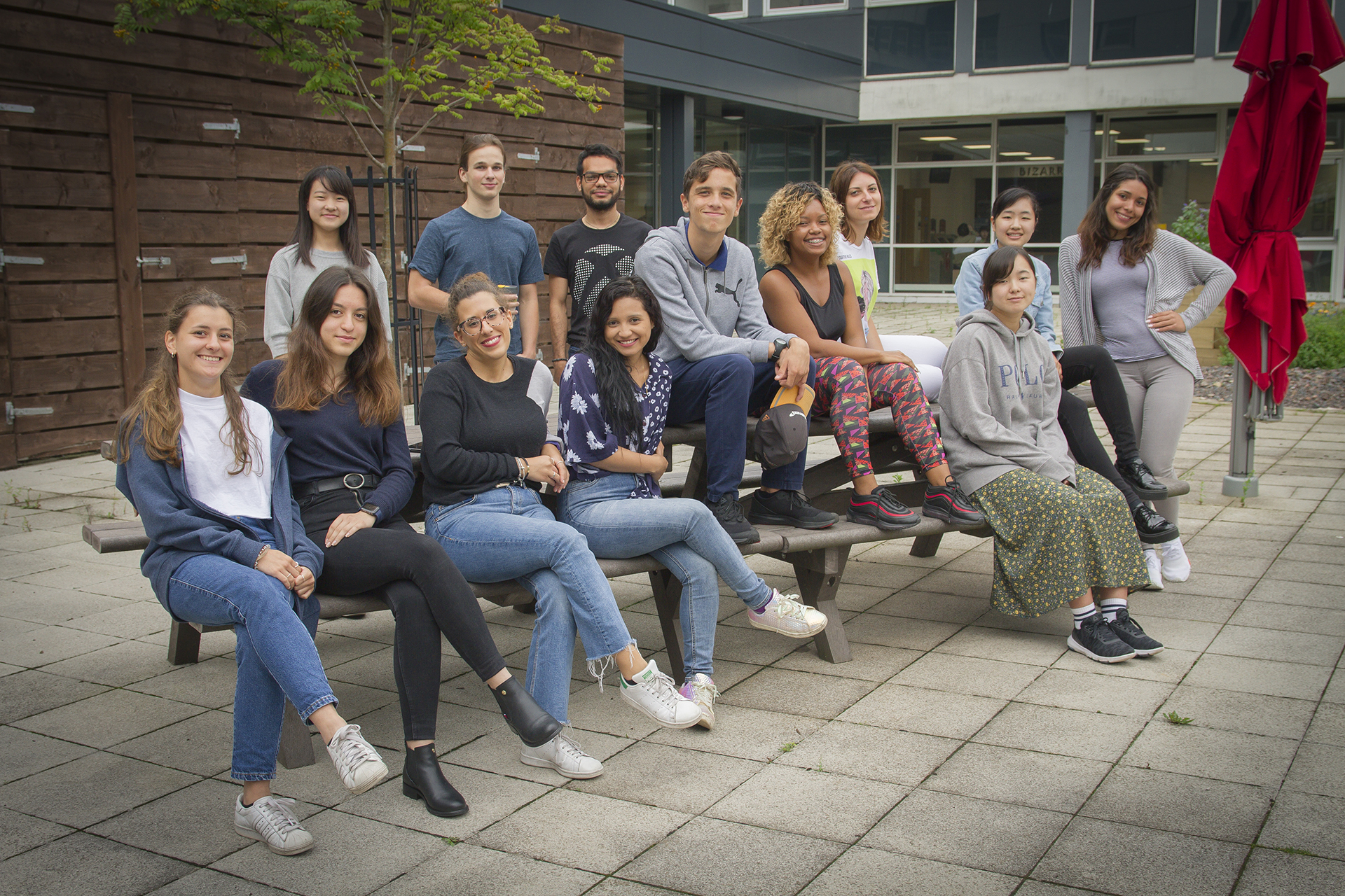 Group of students sitting on a bench, posing for a photo outside a college campus building.