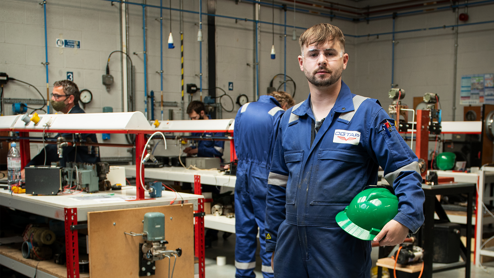Oil and gas student smiling in an engineering classroom, holding their hard hat. 