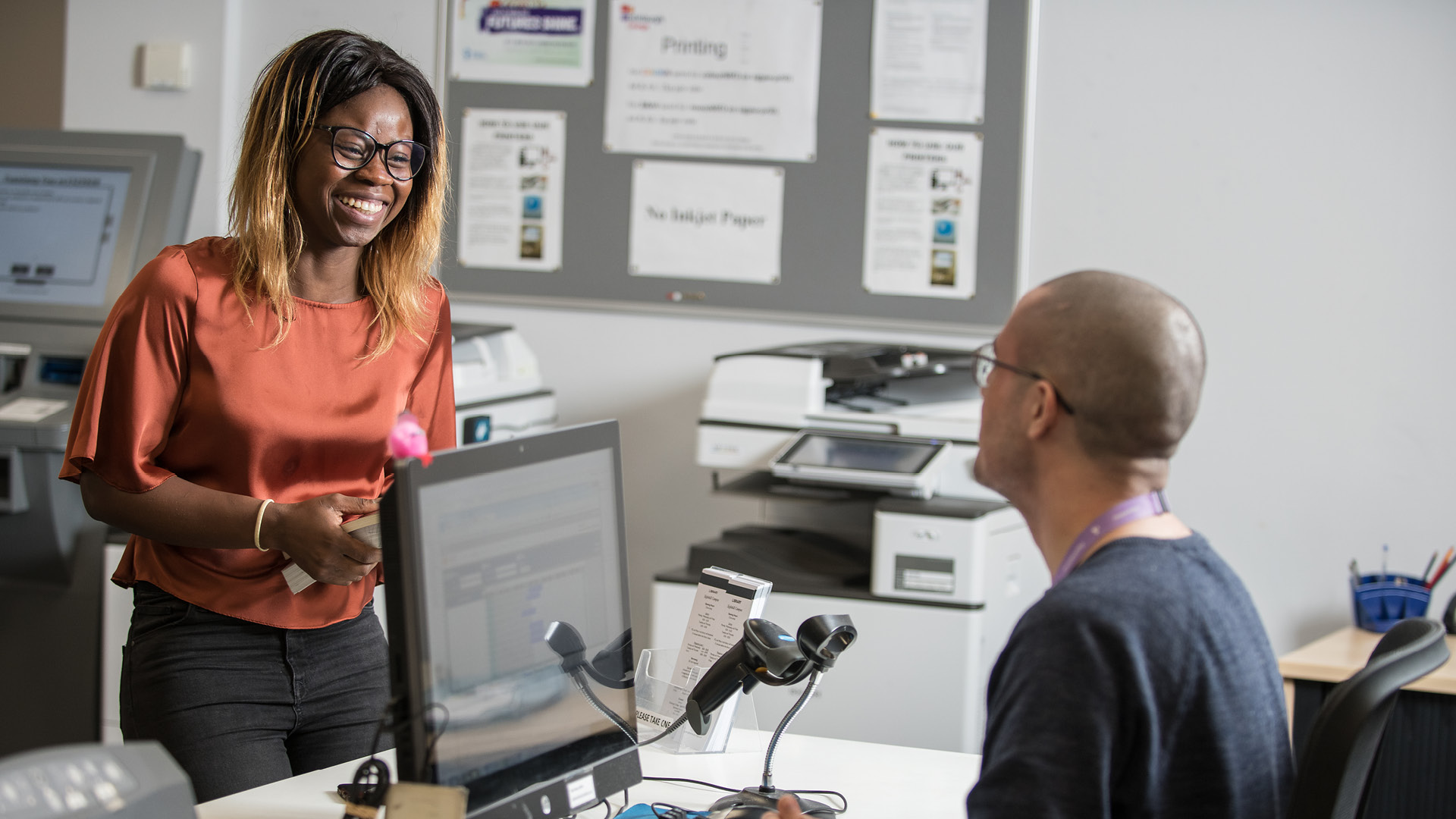Student smiling while they speak to a member of staff in the library.