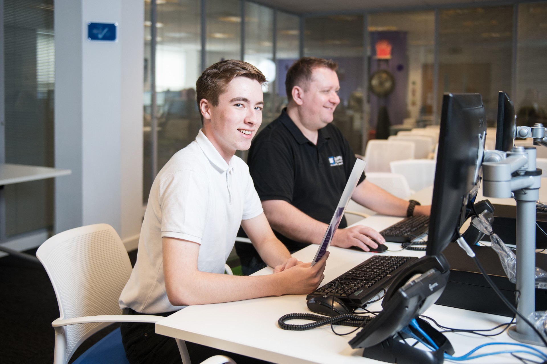 Young student working at a desk in an open plan office during a work placement.