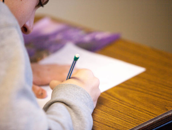 Person crouched over a desk writing on a piece of paper.