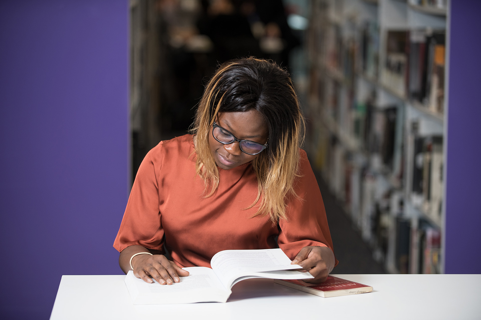 Student in the library reading a book at a desk.