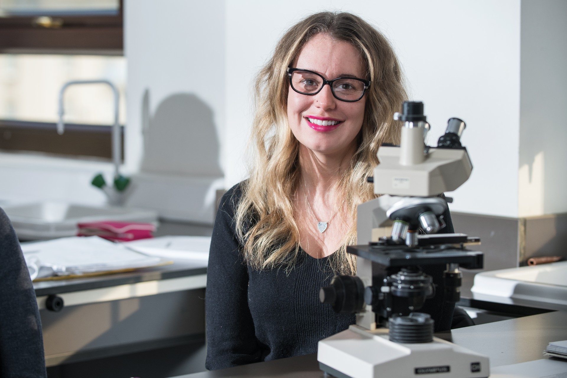 Health professions student sitting next to a microscope in a lab.