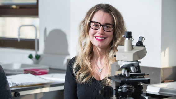 Health professions student sitting next to a microscope in a lab.